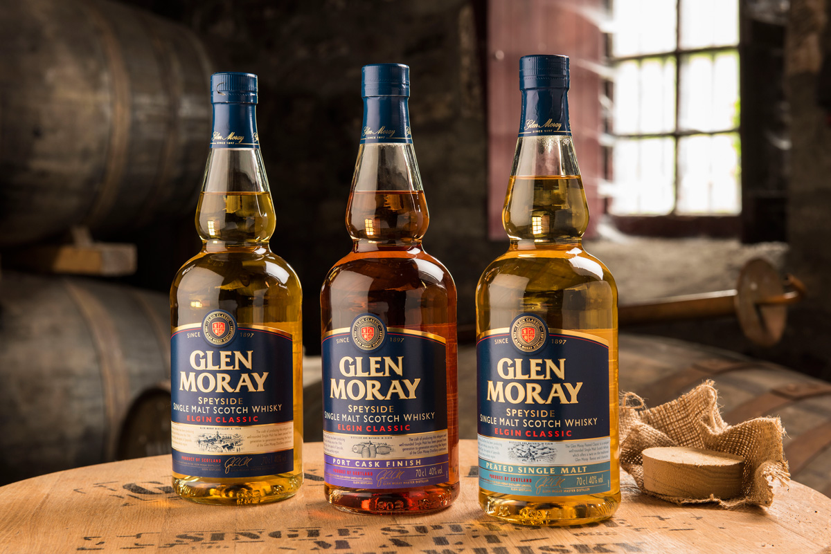 Tre Glen Moray-whiskies i lager. De tre flaskorna är vackert uppställda och ljussatta på ett whiskyfat