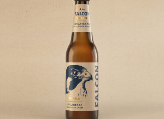 Stående på en kartongfärgad bakgrund med ekologisk känsla, står en Falcon Pilgrim. Ett ekologiskt, ofiltrerat lageröl med något lägre alkoholhalt.