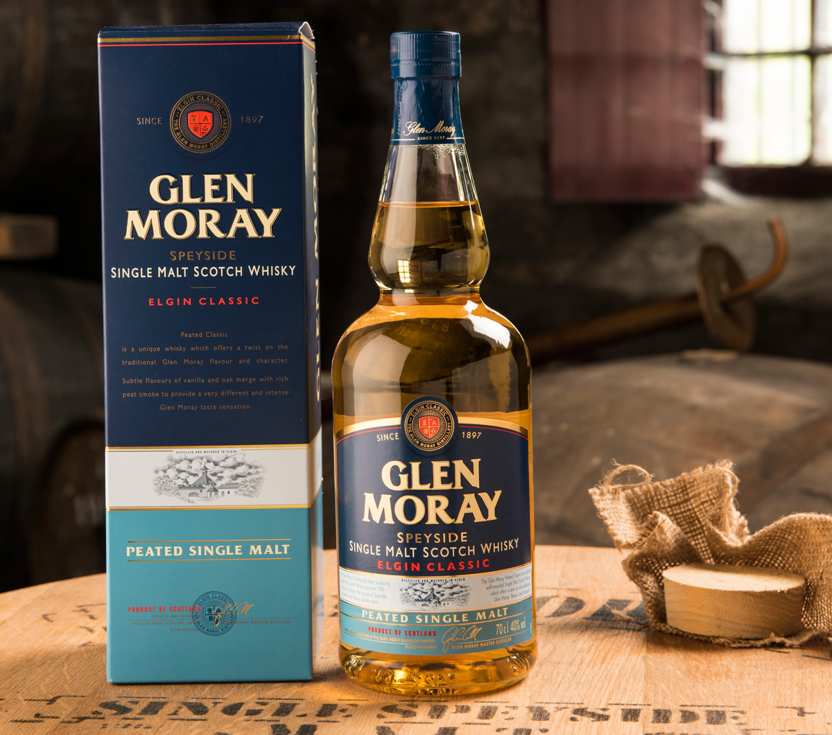 En flaska Glen Moray Peated med kartong ståendes på ett whiskyfat. Vackert, på något varmt vis.